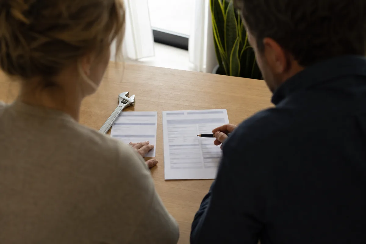 Plombier et cliente examinant un devis détaillé sur une table, attestation d&rsquo;assurance posée à côté